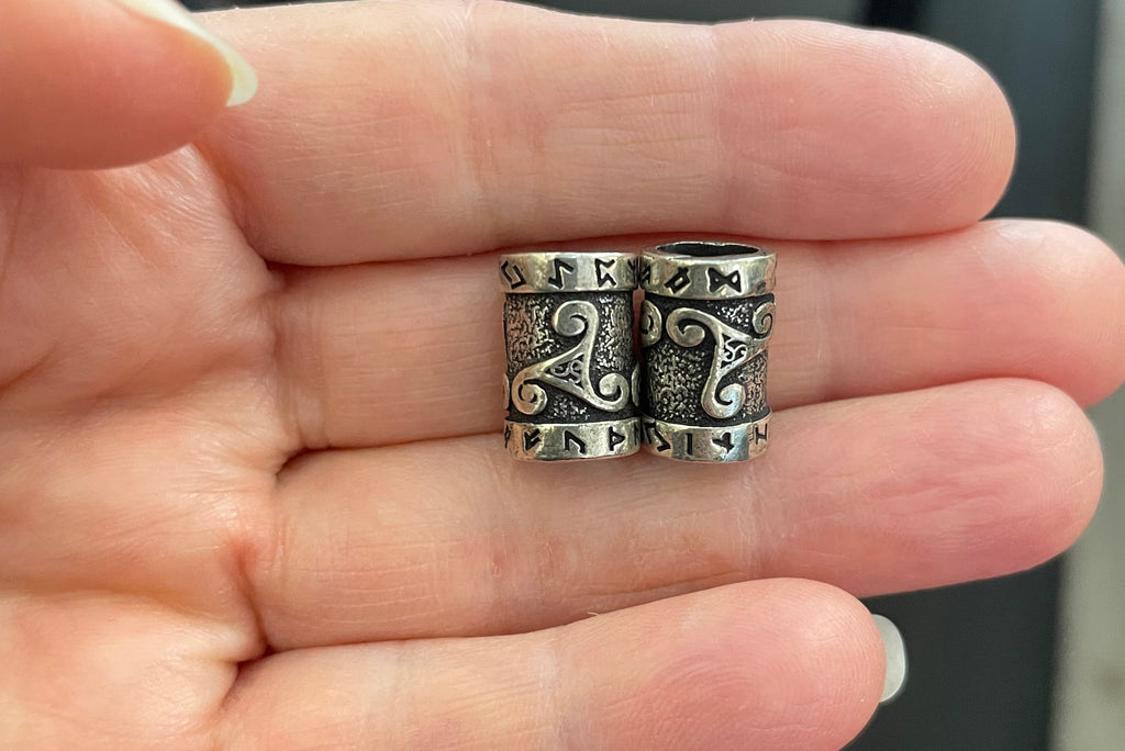 A close-up of a hand holding a small silver-toned cylindrical jewelry piece with engraved scrollwork details.