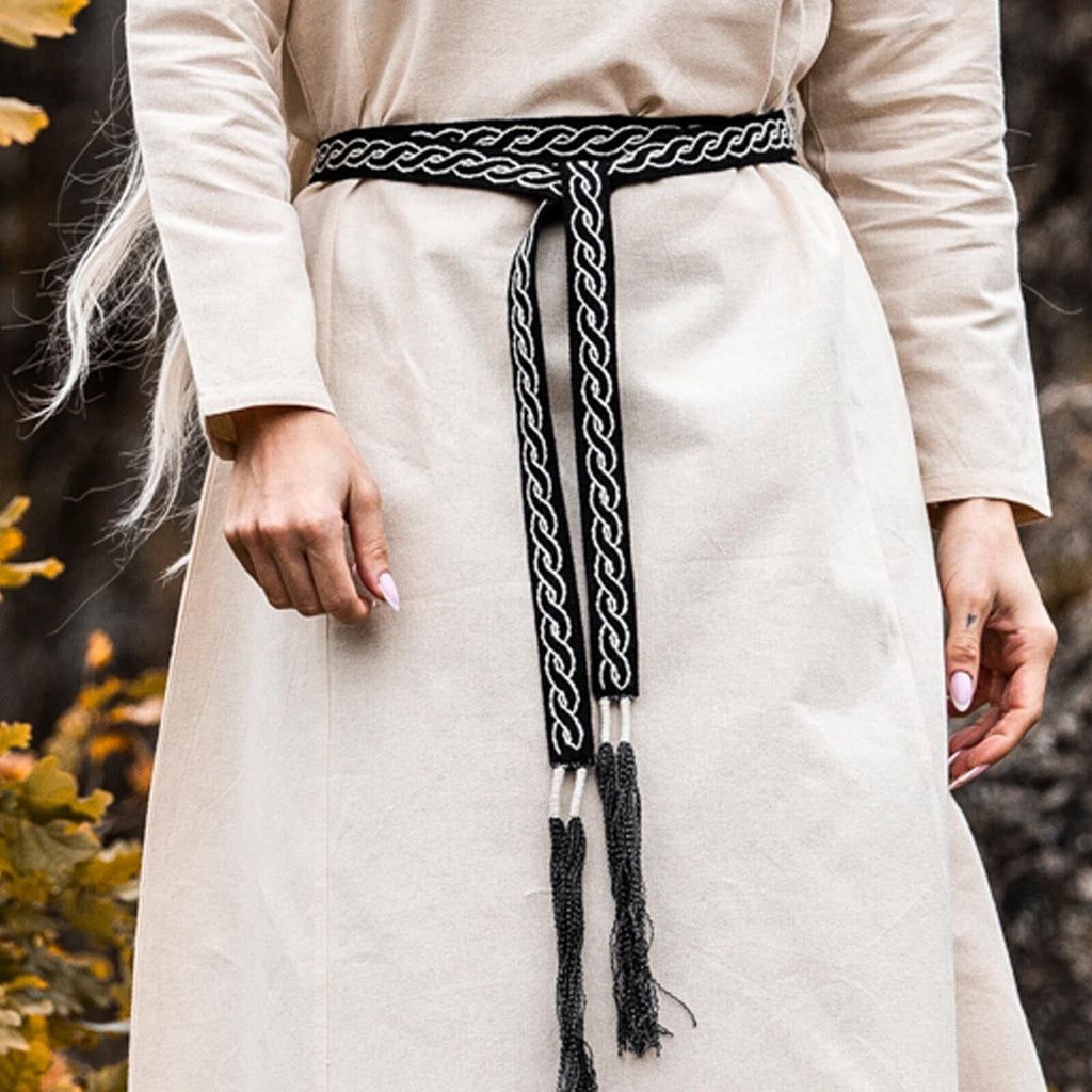 Person wearing a white garment with a braided black belt in a natural setting.