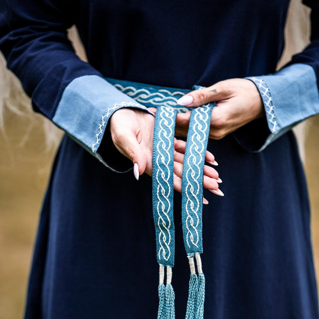 Person holding a blue braided belt with intricate patterns against a neutral background