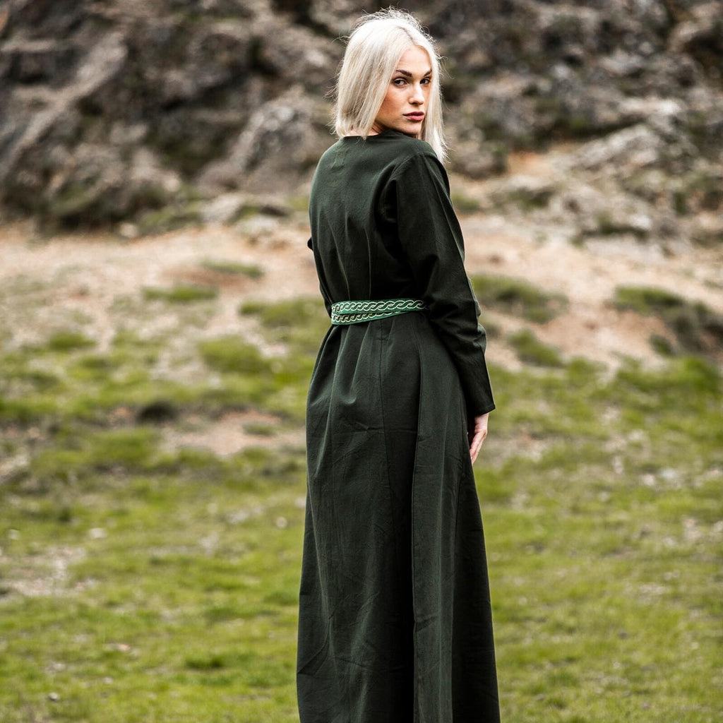 Person wearing a long dark green dress standing in a natural landscape with rocks and grass.