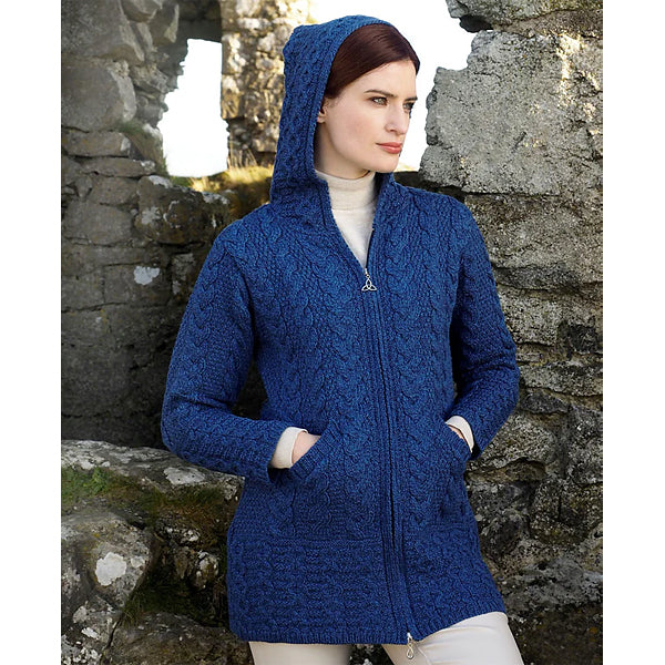 Woman wearing a blue knitted hoodie standing against a stone wall.