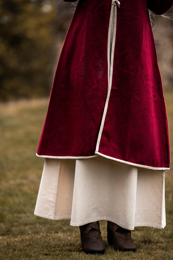 Person wearing a red velvet coat with white trim standing on grass.