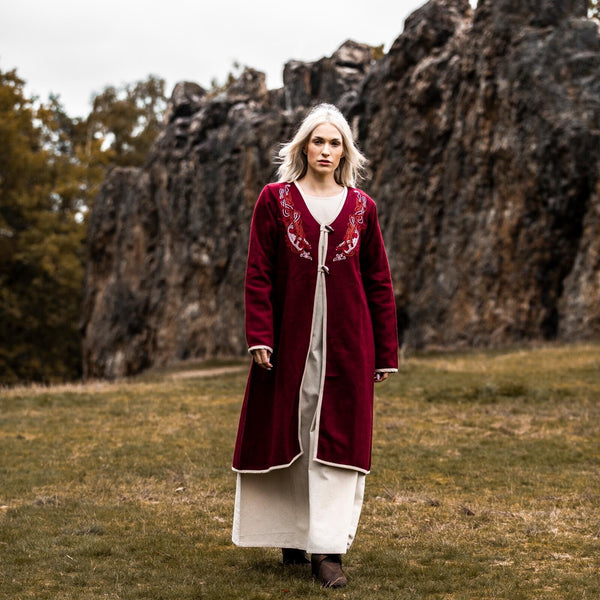 Person wearing a long red coat with white trim standing in a natural landscape.